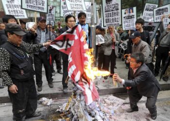 Členovia juhokórejských konzervatívnych občianskych organizácií pália pred japonským veľvyslanectvom v Soule niekdajšiu vlajku cisárskeho Japonska. Protestom reagujú na návštevu japonských zákonodarcov vo svätyni Jasukuni v Tokiu, ktorou podľa nich opätovne rozjatrili rany spôsobené vojnovými krivdami a zločinmi Japonska. FOTO: SITA/Lee Jung-hoon/Yonhap via AP, File