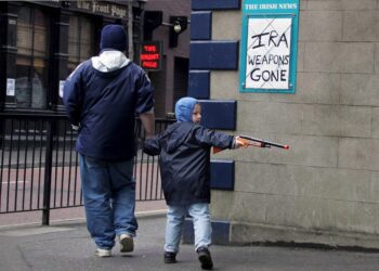 Chlapec s puškou na hraní prochází v roce 2005 v Belfastu kolem plakátku s nápisem "IRA beze zbraní". Irská republikánská armáda (IRA) tehdy zcela odzbrojila a zbavila se zbraní, jimiž po 30 let bojovala za odtržení Severního Irska od Británie. Foto: ČTK /